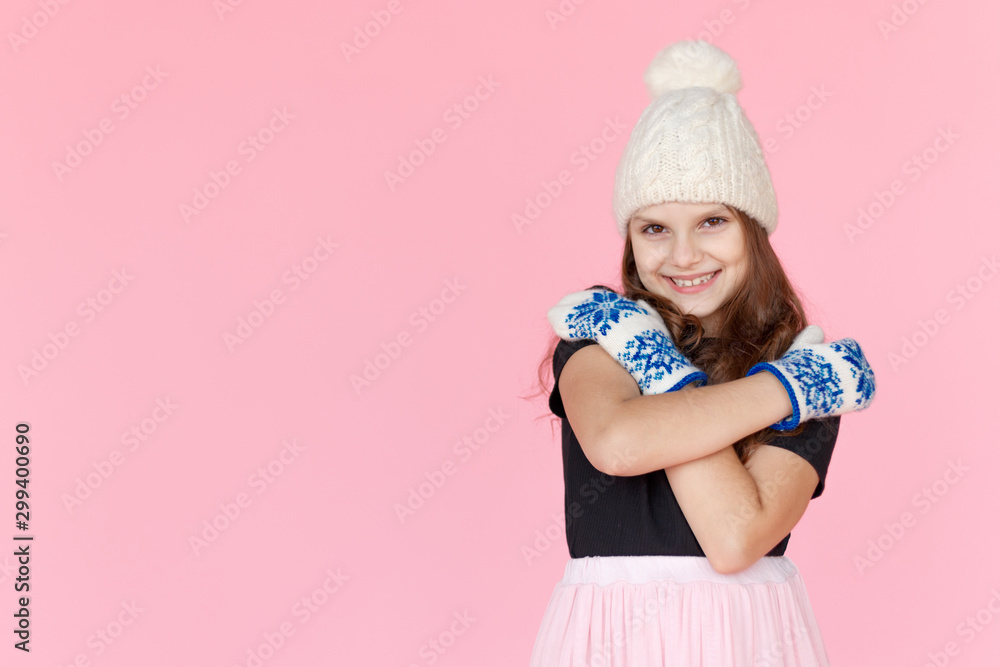 Frontal portrait little girl in white hat and mittens, he embraced with his hands, on pink background in studio. Frontal portrait little girl in white hat and mittens, he embraced with his hands, on pink background in studio.
