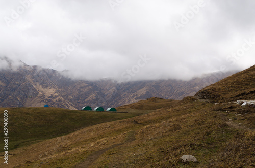 Forest camp houses in the himalayan mountains with cloud covered brown mountains in the background © deadmanswill