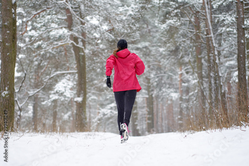 Woman wearing pink sport outfit runing in winter forest, view from back