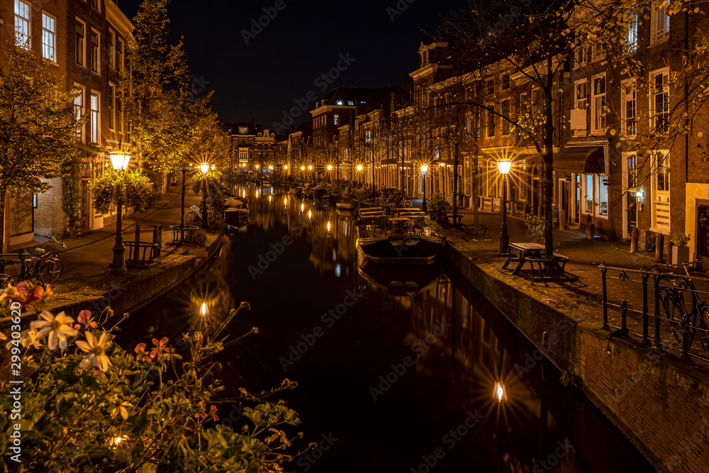 A night shot from the Sint Jansbrug on the Oude Rijn with numerous boats and illuminated old canal-side houses, Leiden, the Netherlands