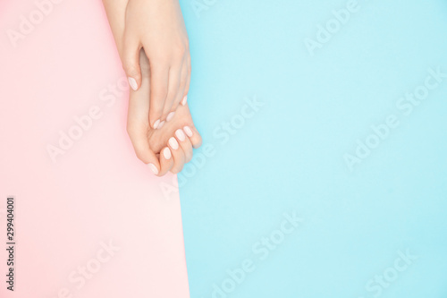 Fototapeta Naklejka Na Ścianę i Meble -  Beautiful female hands with stylish nail manicure gel polish on pink and blue background, top view. Skin care concept