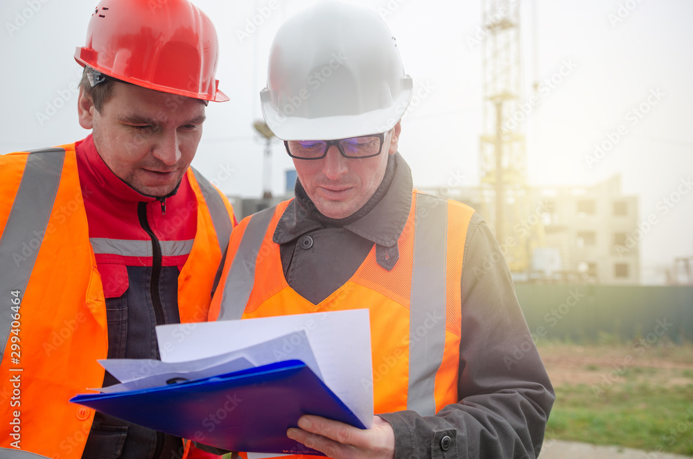 Fototapeta premium An engineer with a hard hat and helmet discussing a project at a construction site with a team leader in autumn or winter. architecture construction concept. Industrial safety