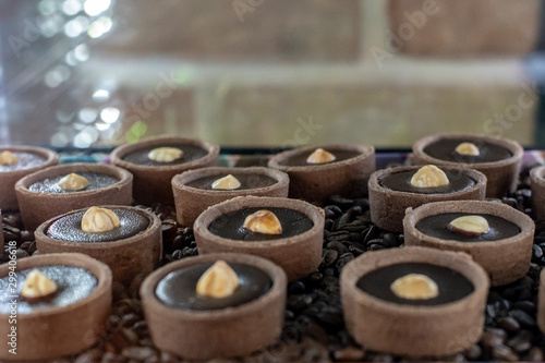Round chocolate muffins in tartlets with hazelnuts in the middle stand in the refrigerator on a tray among coffee beans