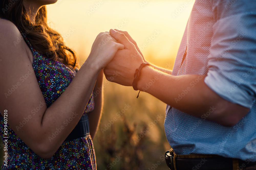 Holding hands loving couple stands in the middle of the wheat field at sunrise. A young couple in love touched hands on the first date. Loving couple has a happy relationship. First love concept.