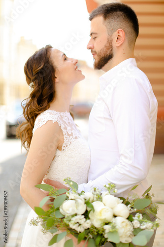 Happy groom hugging fiancee keeping flowers and wearing white dress.