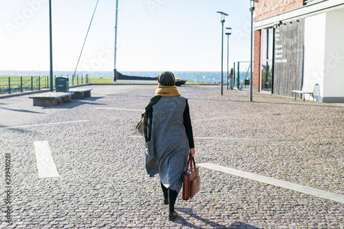 Fotografie Woman wearing headscarf walking by ocean with briefcase