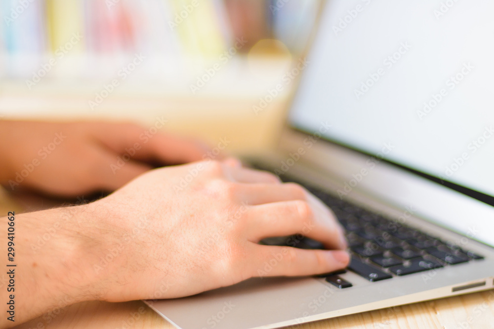 Close up hands multitasking man using notebook computer in library Close up hands multitasking man using notebook computer in library
