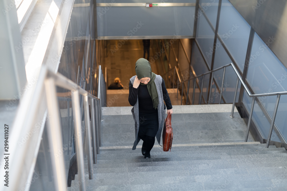 Woman wearing headscarf walking up stairs with briefcase