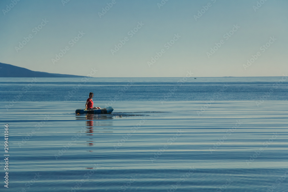 Naklejka premium A girl swims in a boat on the White Sea, in summer, at sunset. Kola Peninsula, Kandalaksha.