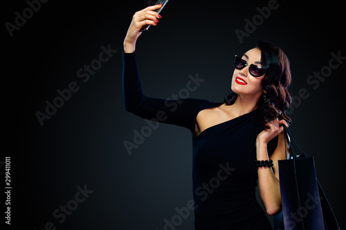 Shopping on Black Friday and Cyber Monday. Sale concept for shops. Woman holding bag and making selfie on smartphone, isolated on dark background