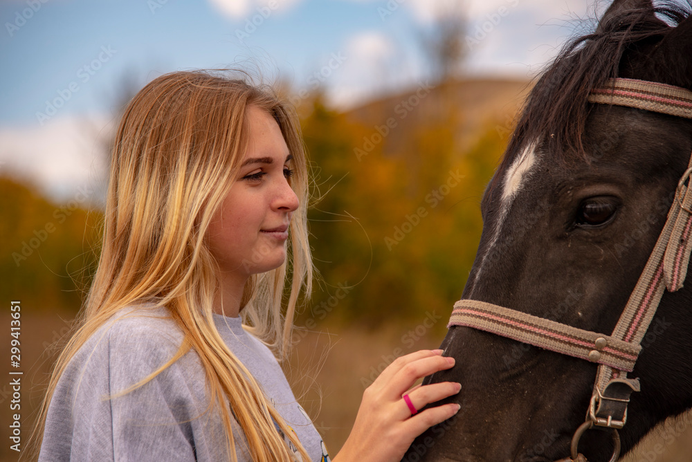 Obraz premium A young girl with blond hair gently strokes the brown horse's muzzle.