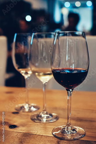 Close up image of three glasses with red and white wine, on wooden table, served for wine tasting event. Blurred background. Bar or restaurant interior, subdued light. Selective focus, film grain effe