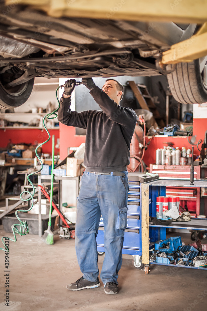 Auto mechanic repairer checking condition under car on vehicle lift