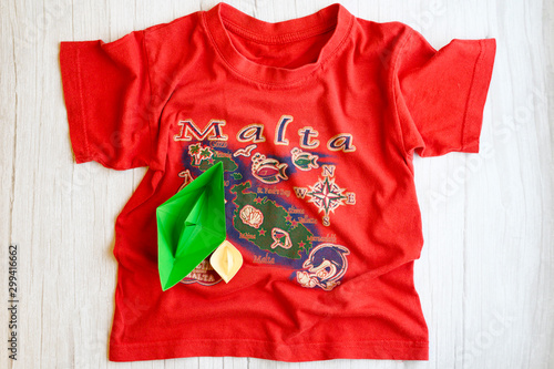origami paper boat is located on a children's t-shirt with the island of Malta depicted on it. The concept of ship travel
