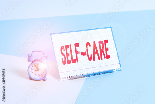 Word writing text Self Care. Business photo showcasing practice of taking action to preserve or improve ones own health Mini size alarm clock beside a Paper sheet placed tilted on pastel backdrop