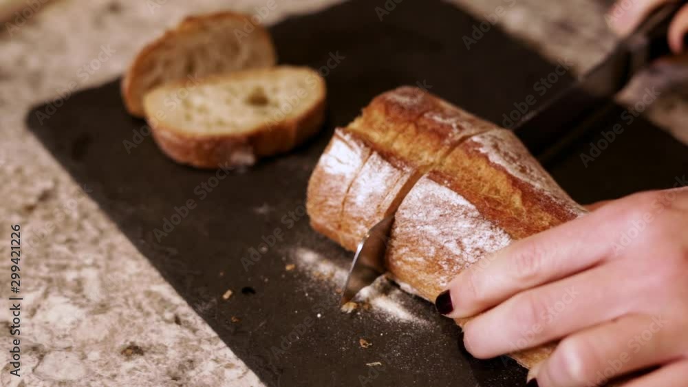 Very shallow depth of field Slow motion HD woman cutting home made organic baguette bread and slicing it into pieces on cutting board Very shallow depth of field Slow motion HD woman cutting home made organic baguette bread and slicing it into pieces on cutting board