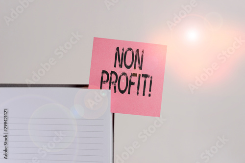 Text sign showing Non Profit. Business photo showcasing not making or conducted primarily to make profit organization Upper view lined hard cover note book sticky note inserted clear background photo