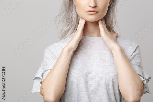 Female checking thyroid gland by herself. Close up of woman in white t- shirt touching neck with red spot. Thyroid disorder includes goiter, hyperthyroid, hypothyroid, tumor or cancer Health care. photo
