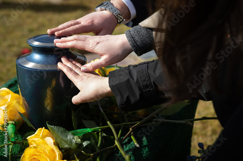Three hands touching a cremation urn at a funeral