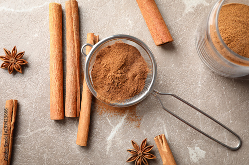 Cinnamon sticks, powder and sieve on grey background, top view