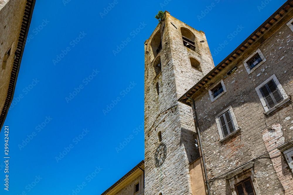 The Palazzo del Podestà, in Piazza dei Priori in the ancient medieval village of Narni. The stone bell tower and the clock. Umbria, Terni, Italy. The blue sky on a summer day.