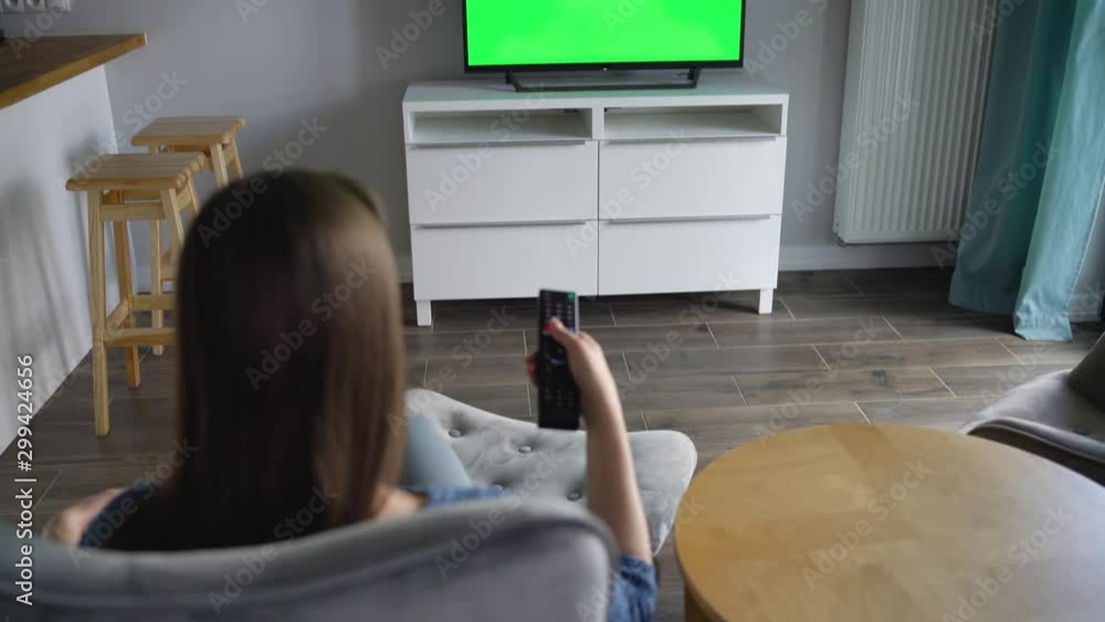Vidéo Stock Woman is sitting in a chair, watching TV with a green