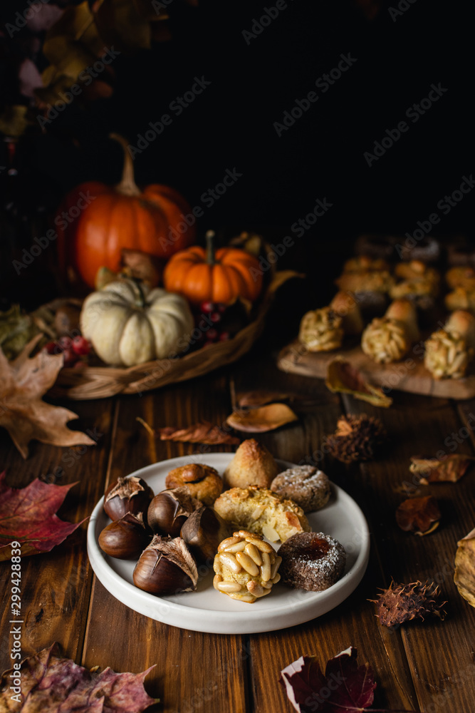 All Saints Day marzipan sweet panellets and roasted chestnuts, autumn leaves on wooden table All Saints Day marzipan sweet panellets and roasted chestnuts, autumn leaves on wooden table