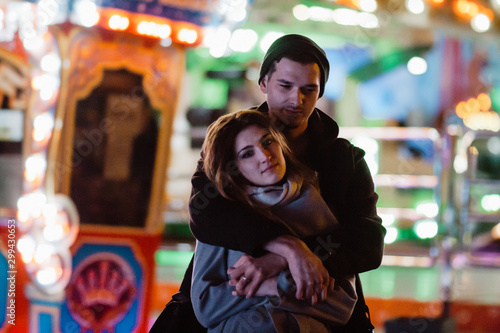 Photo of a smiling loving couple walking outdoors in amusement park having fun hugging in the evening