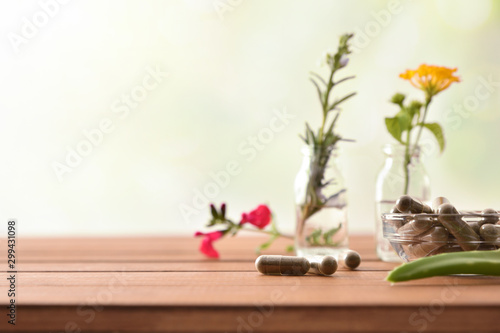 Natural herbal medicine capsules on table with vials and plants