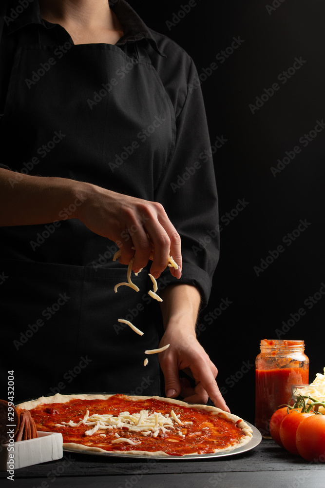 Chef cooks pizza, sprinkled with mozzarella cheese, freezing in motion on the background with ingredients. Recipe book, menu, home cooking. Vertical frame