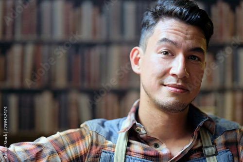 Man with a slight smirk sitting in front of a book shelf with copy space to the left photo