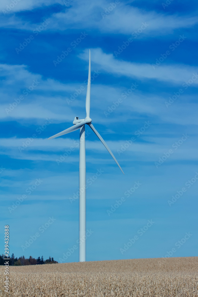 View of a giant wind power generator on an autumn agricultural field landscape with a blue sky background View of a giant wind power generator on an autumn agricultural field landscape with a blue sky background