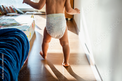 Photographie Baby in diapers learning to walk in her bedroom barefoot.
