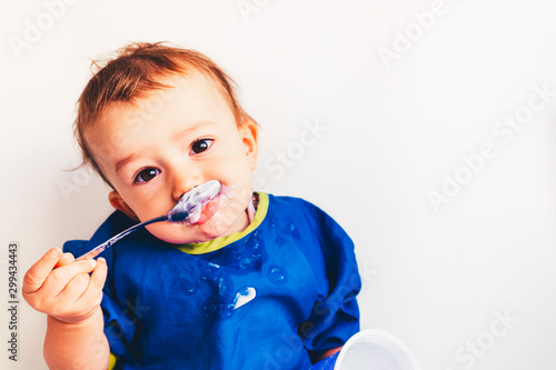 Baby savoring his first yogurt with a spoon, with a spotted face and adorable expression. photo