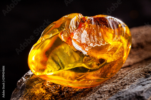 Natural amber. A piece of yellow transparent natural amber on large piece of dark stoned wood.