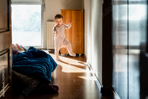 Fotografija Newly awake baby in pajamas takes her first steps in the bedroom.
