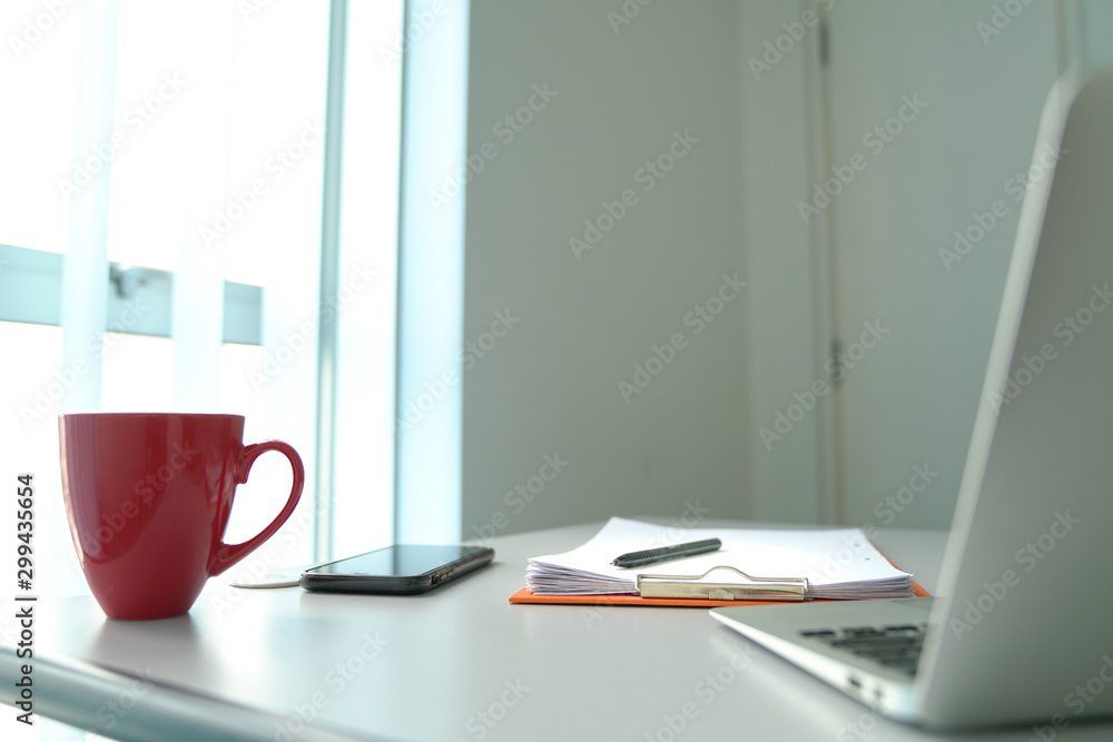Office table next to windows. Computer, cell phone, coffee cup and focus on clipboard. Office table next to windows. Computer, cell phone, coffee cup and focus on clipboard.