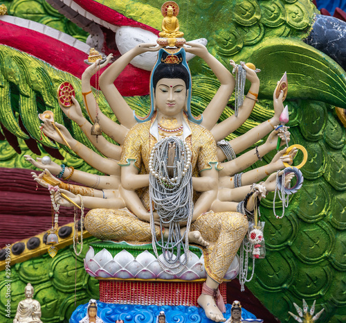 Ko Samui Island, Thailand - March 18, 2019: Wat Laem Suwannaram Chinese Buddhist Temple. Small Guan Yin under giant statue with 18 arms and pearl necklaces in her hands. Green dragon skin in back. photo