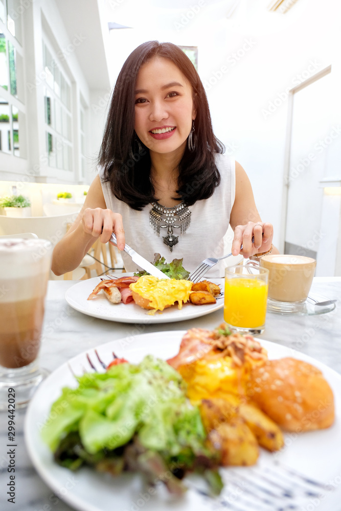 Young woman eating Breakfast - fried egg, beans, tomatoes, mushrooms, bacon and toast.