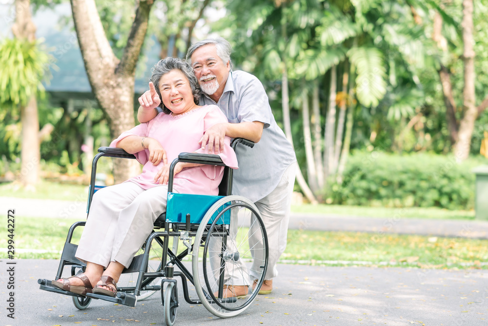 Happy senior woman in a wheelchair walking with her husband Happy senior woman in a wheelchair walking with her husband