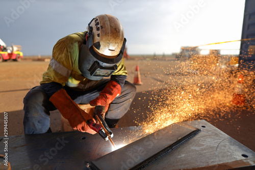 Construction worker wearing ears plug  helmet, red welding leather glove protection while commencing hot work gouging metal plate on the ground surface    photo