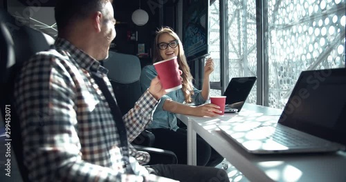 Young office male and lady workers drinking coffee during break and chatting, sitting at desk, female flirting, affair