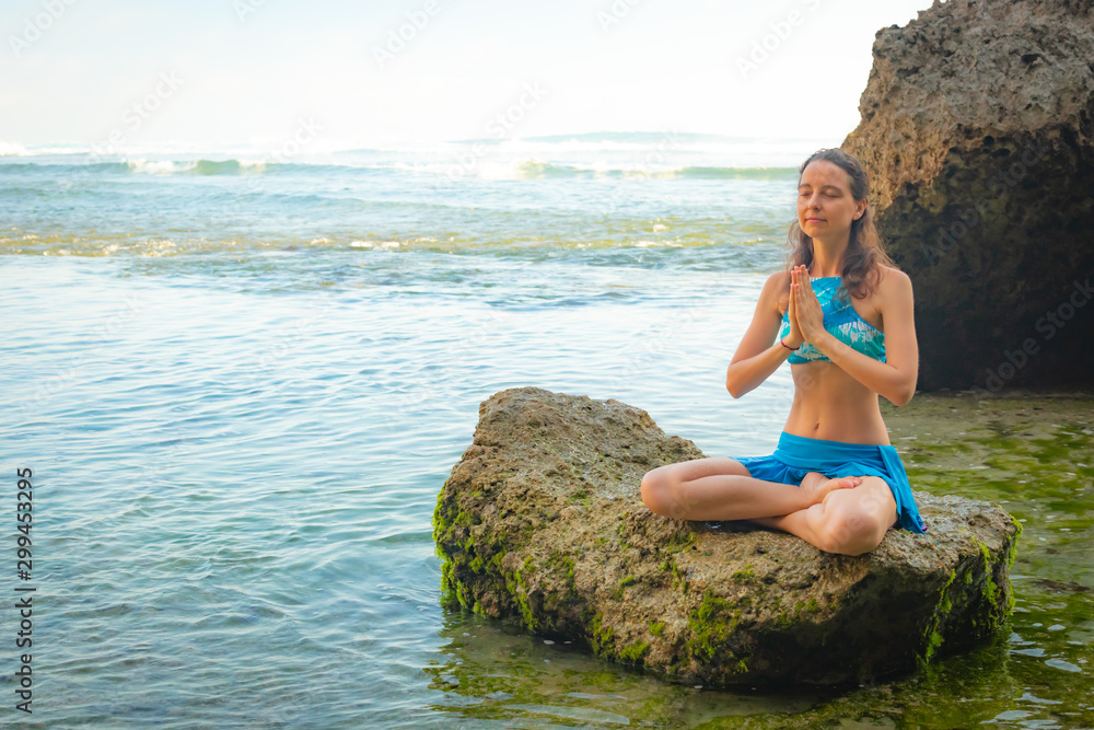 Young woman sitting on the rock, meditating, practicing yoga and pranayama at the beach, Bali. Hands in namaste mudra Young woman sitting on the rock, meditating, practicing yoga and pranayama at the beach, Bali. Hands in namaste mudra