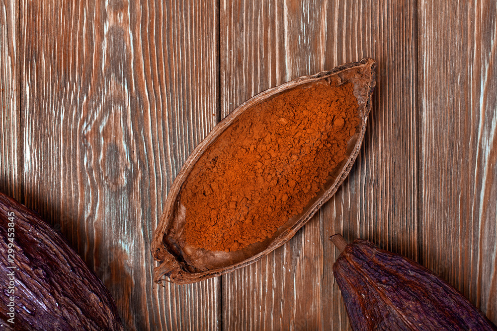 Cacao powder in a natural cocoa pod on a old wooden background. Top view.