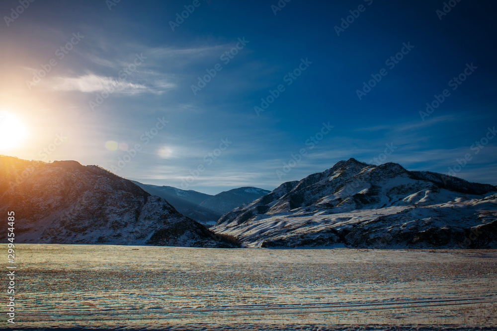 Fototapeta premium Fantastic panorama of snow-covered plains and mountain slopes covered with snow on a frosty sunny winter day. Wild and desert places, road trips, Siberian expanses.