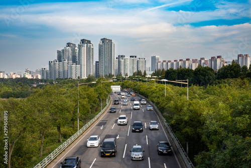 Urban car road scenery with buildings and green spaces.