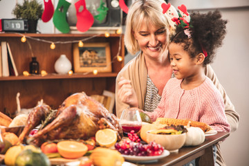 Little Girl Eating  and smile Thanksgiving Celebration Concept. grandmother and granddaughter eating  and smile  at freshly prepared turkey for thanksgiving dinner.
