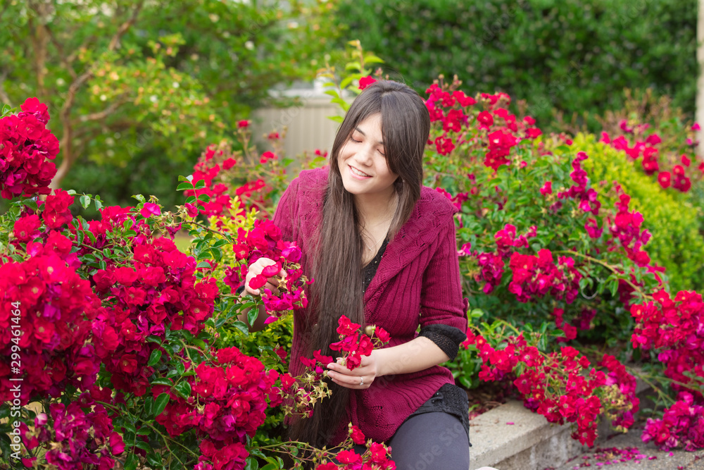 Young woman sitting in red rose bushes picking flowers Young woman sitting in red rose bushes picking flowers