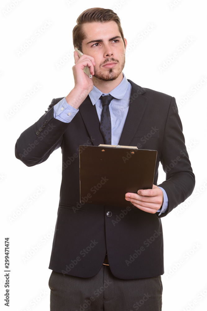 Young bearded businessman in suit using phone and holding clipboard Young bearded businessman in suit using phone and holding clipboard
