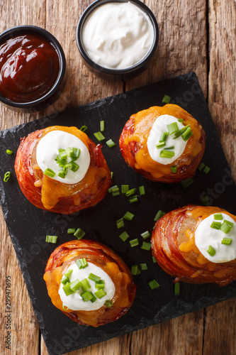 Baked potatoes wrapped in bacon topped with cheese and sour cream close-up. Vertical top view